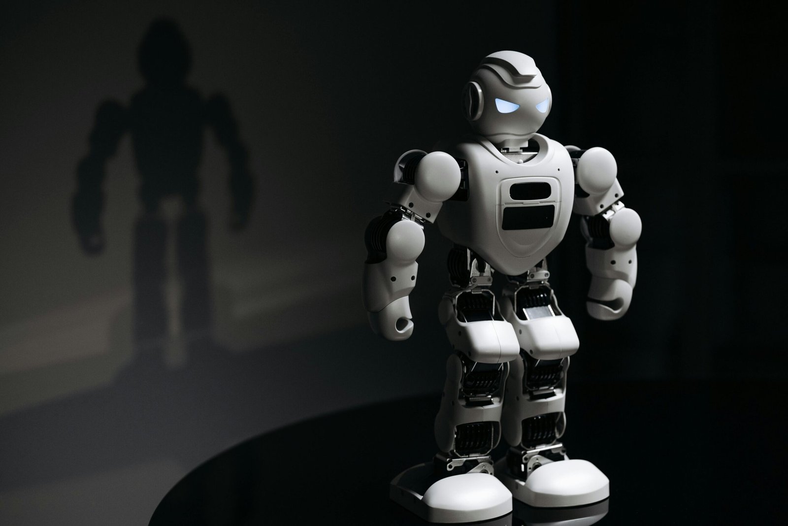 White robot toy casting a shadow in a dark studio setting, highlighting artificial intelligence.