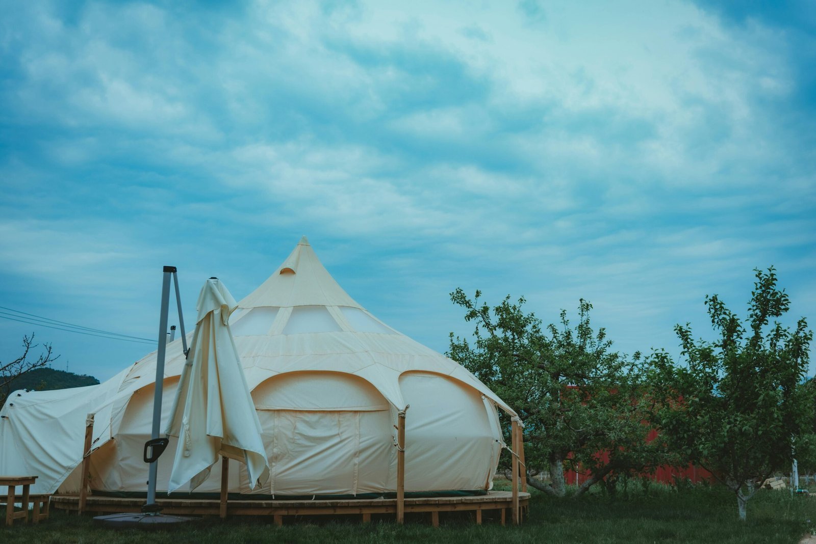 A beautiful cream-colored glamping tent set amid lush green trees under a vibrant blue sky.