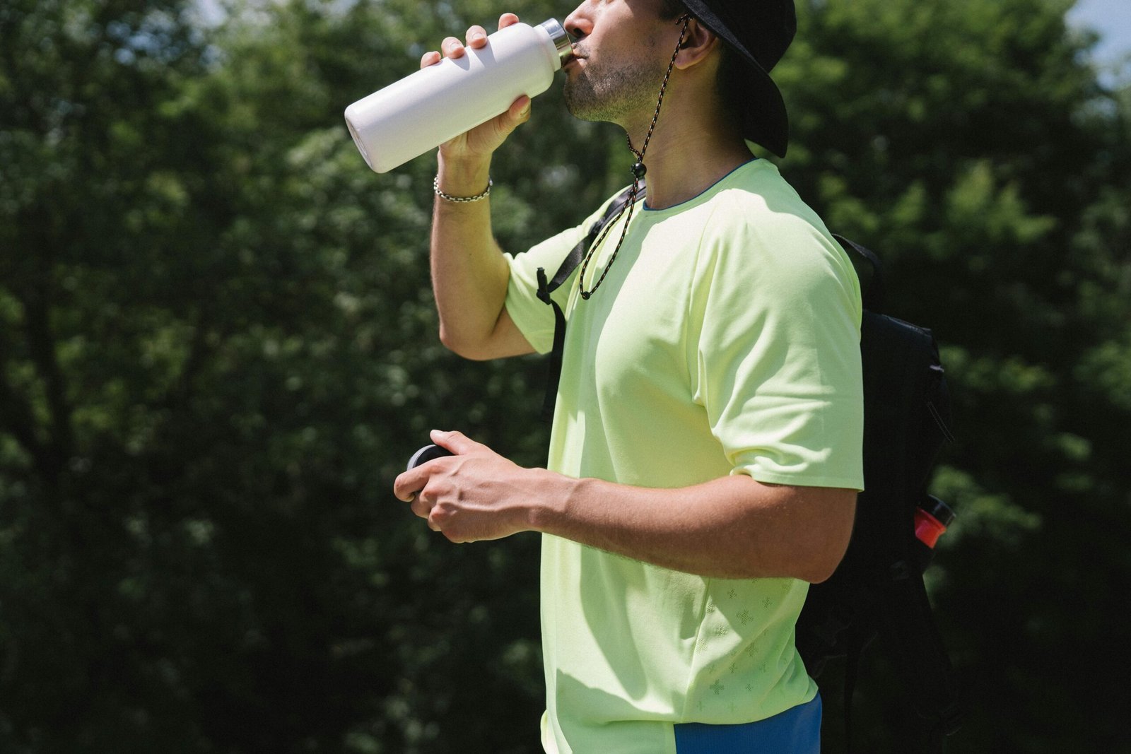 Adult man staying hydrated while hiking outdoors on a bright and sunny day.