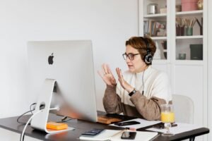 Professional woman wearing headphones conducts video call in a modern workspace, focused on communication.