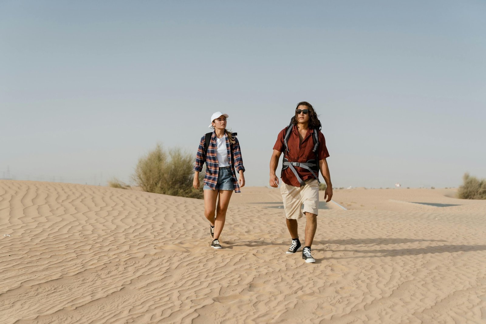 Couple exploring sand dunes in casual wear on a sunny day.