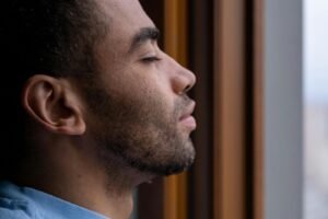 Side profile of a man with closed eyes enjoying a calm moment by the window.