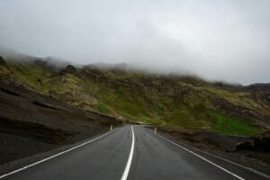 A foggy mountain road in Iceland, offering a serene travel scene with lush green hills.
