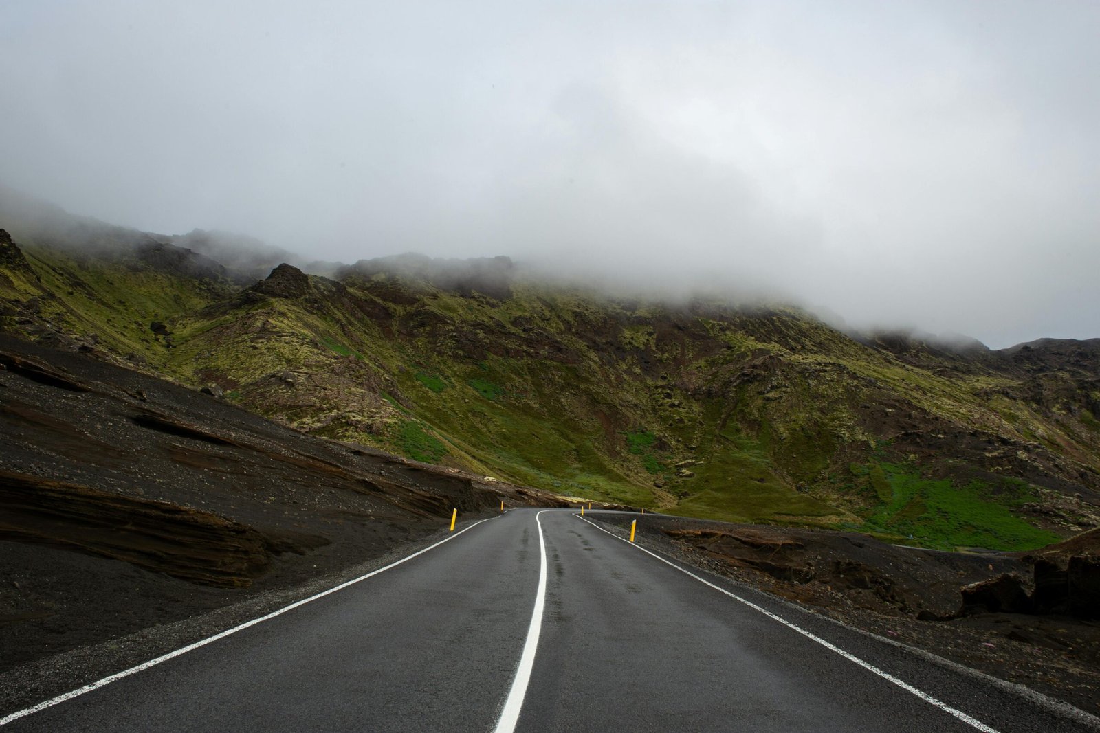 A foggy mountain road in Iceland, offering a serene travel scene with lush green hills.