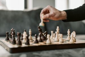 Artistic close-up of a hand moving a chess piece on a chessboard in a cozy setting.