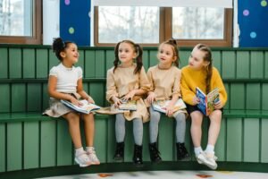 Four girls sitting indoors reading books, fostering a love for learning and education.