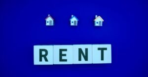 Miniature houses above letters spelling 'RENT' on a blue background, ideal for real estate themes.