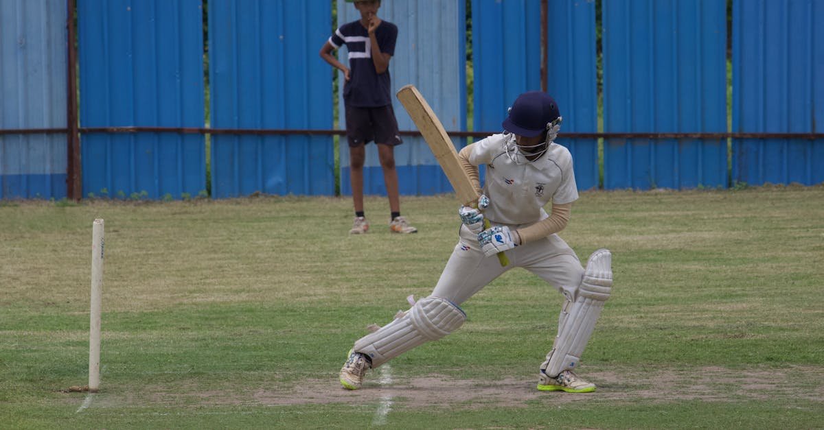 Cricket player batting on a grass field in Gahunje, India, showcasing dynamic sports action.