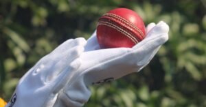Detailed photo of a red cricket ball held by gloved hands outdoors.