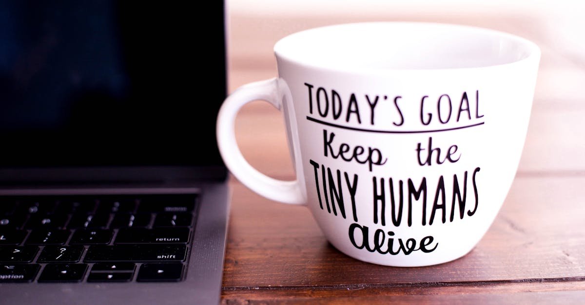 Close-up of a mug with motivational text beside a laptop on a wooden desk.
