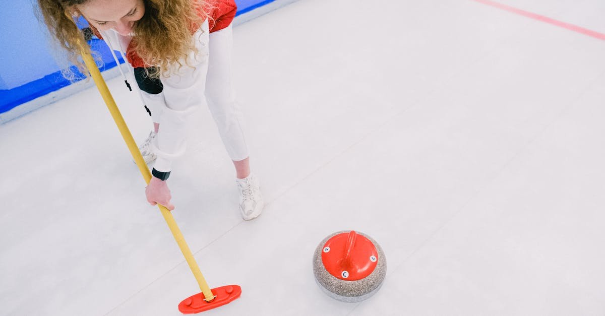 Aerial shot of woman playing curling indoors, sweeping ice beside a curling stone.