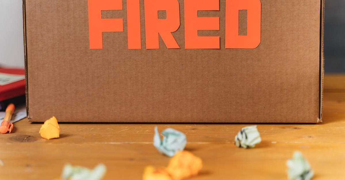 Close-up of a cardboard box labeled FIRED on a wooden table with crumpled papers.
