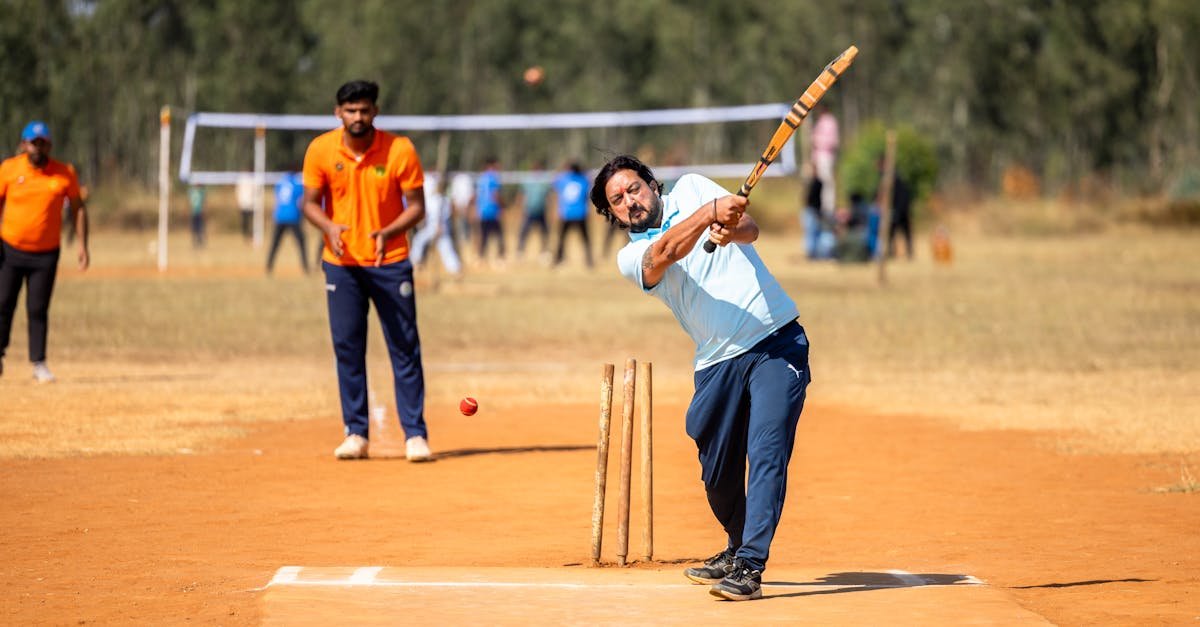 A cricket player in mid-swing during an outdoor match on a sunny day.