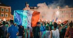 Vivid night-time celebration in France with crowds waving flags in city square.