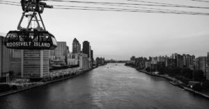 Black and white view of Roosevelt Island tram crossing the East River with a city skyline backdrop.