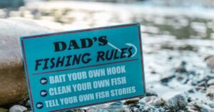 A close-up of a fun sign highlighting dad's fishing rules placed by a river, perfect for Father's Day.