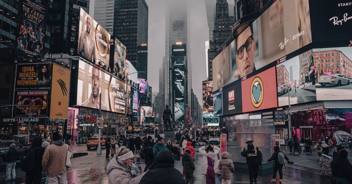 Crowds at Times Square surrounded by towering billboards and skyscrapers on a cloudy day.