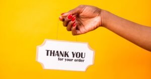A hand holding a thank you sign on a bright yellow background, expressing gratitude.