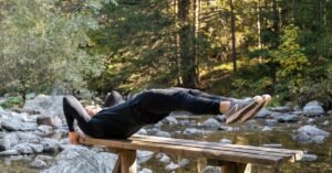 Man performing a core exercise on a bench by a serene river in a forest setting.