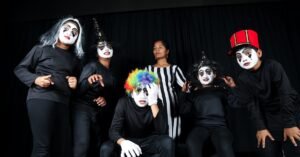 A group of young performers in vibrant costumes and masks showcasing a theatrical performance indoors.