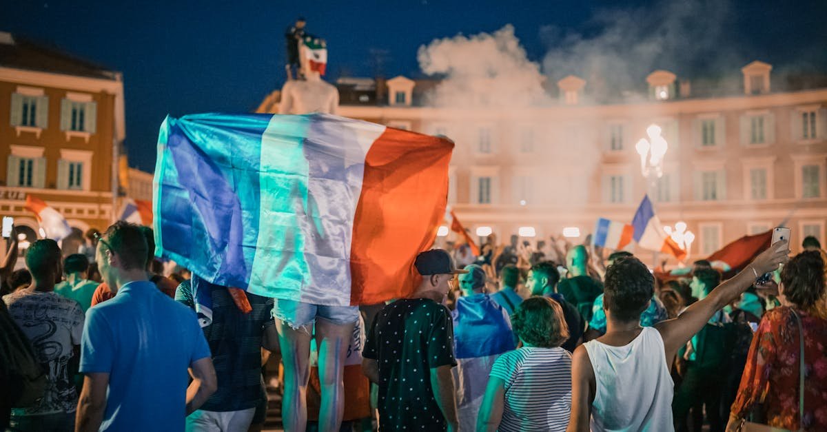 Vivid night-time celebration in France with crowds waving flags in city square.