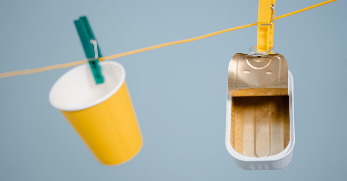 An artistic display of a yellow cup and can hanging on a clothesline with pegs against a blue background.