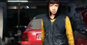 Teenage mechanic working in a Gaziantep car garage, wearing a hoodie and vest.