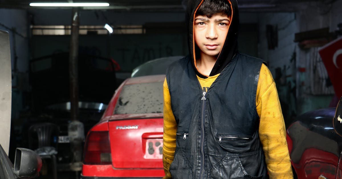 Teenage mechanic working in a Gaziantep car garage, wearing a hoodie and vest.