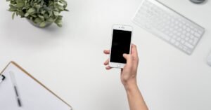 A clean and minimalist home office setup featuring a smartphone, keyboard, and plant.