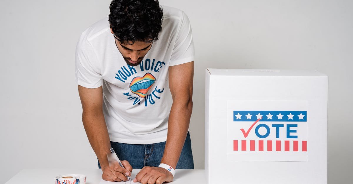 A man writes on a paper to cast his vote next to a ballot box in a studio setting.