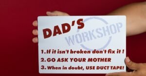 Close-up of a humorous sign with Dad's workshop rules on a red background held by hands.