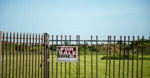 A large plot of land bordered by an iron fence, complete with a 'For Sale' sign in Miami, FL. Ideal for development.